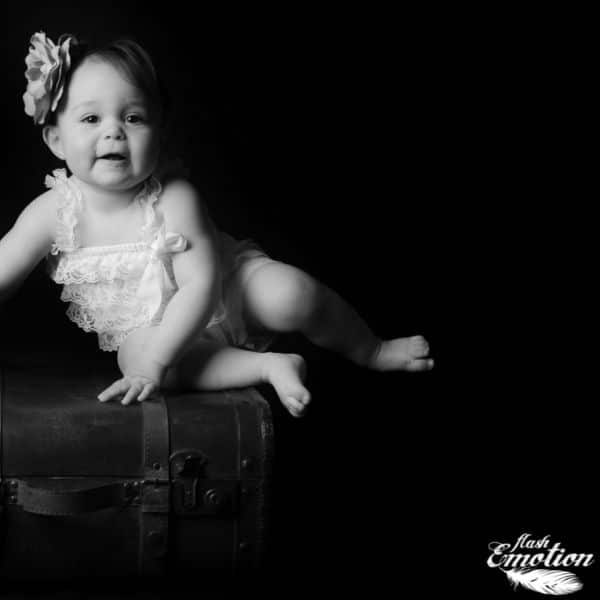 Photographie en noir et blanc d'un bébé assis sur une malle